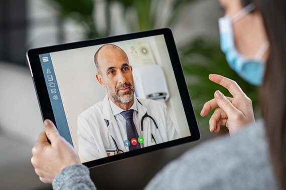 patient wearing a mask on tablet in conference call with doctor